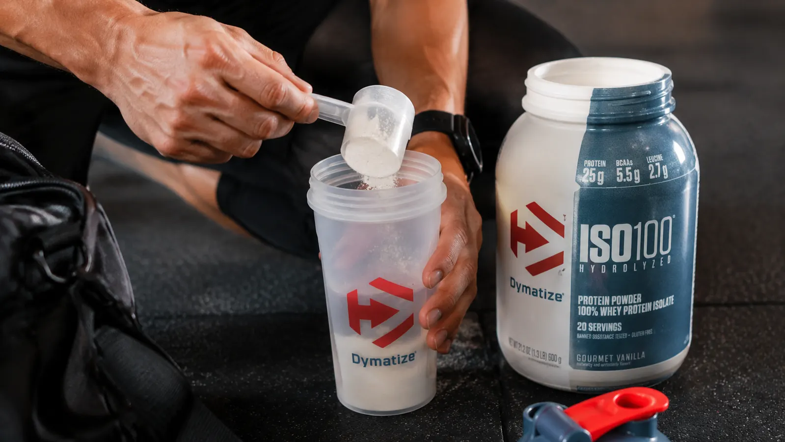 Person scooping whey isolate powder into a shaker cup after a workout