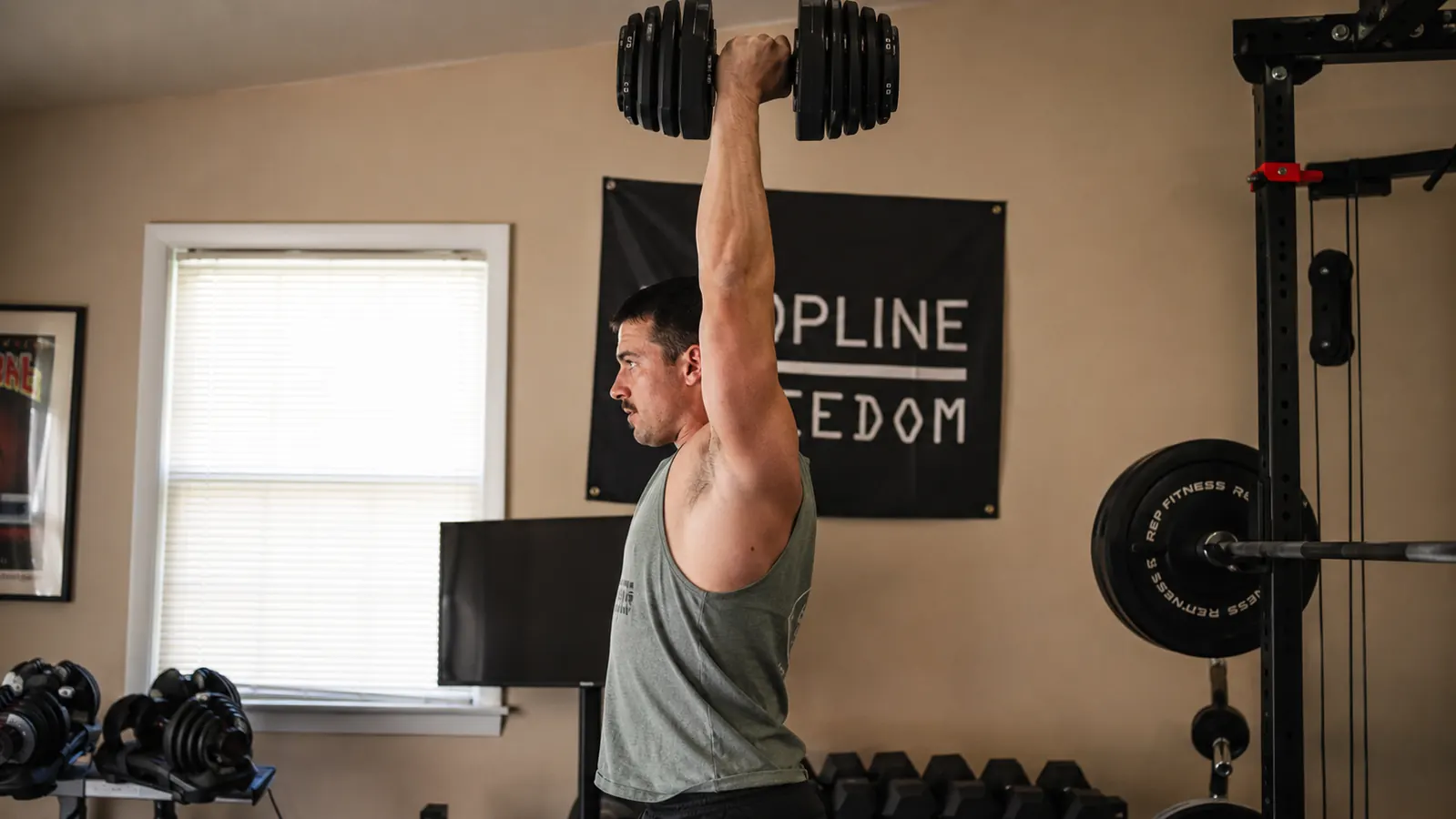 Person pressing a FEIERDUN DS2 dumbbell at the 70-pound setting in a home gym, arm extended, face showing focused effort