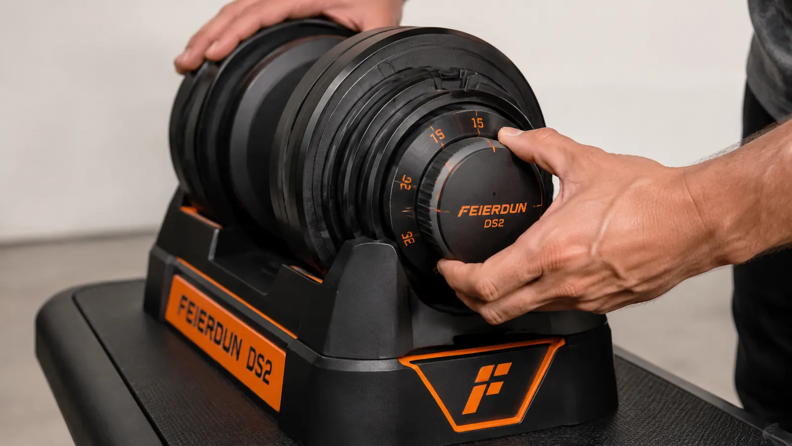 Hand gripping a FEIERDUN DS2 dumbbell handle showing the selector dial turned to 25 pounds