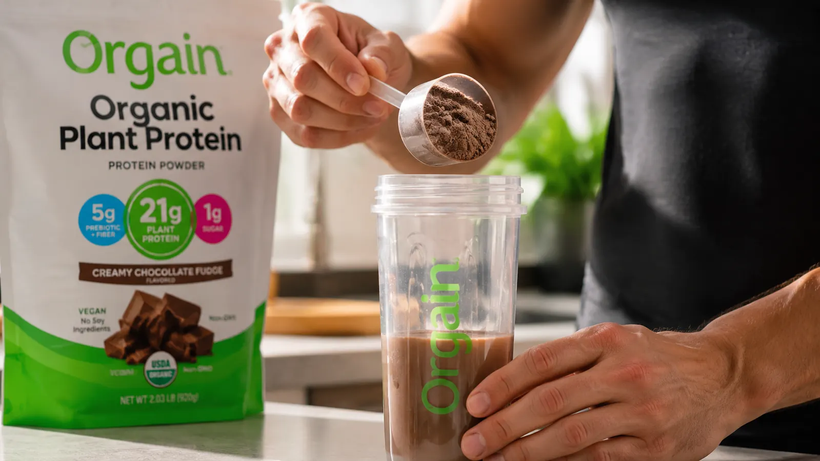 Hand scooping Orgain plant protein powder into a blender bottle