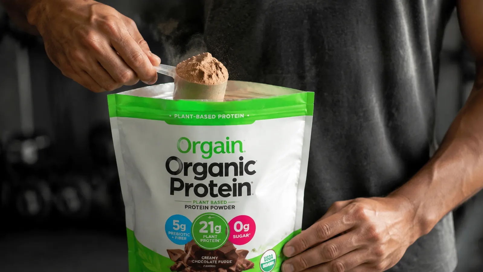 Hand scooping Orgain vegan protein powder from bag showing chalky brown powder texture