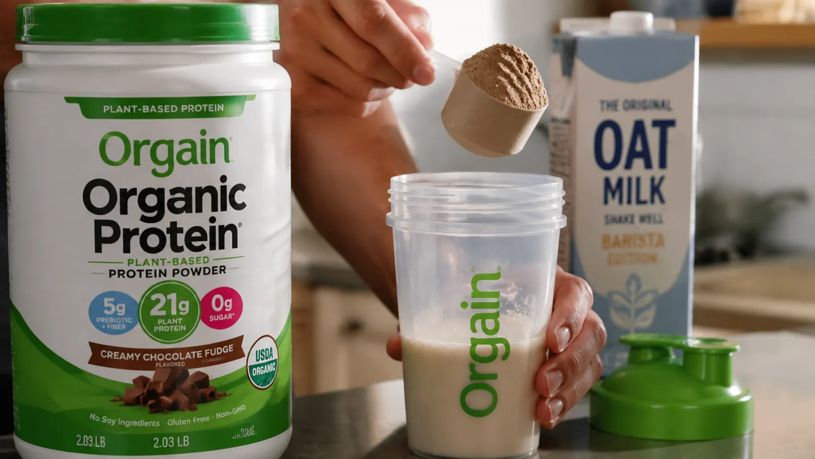 Hand scooping Orgain plant protein powder into a shaker cup with oat milk carton in the background