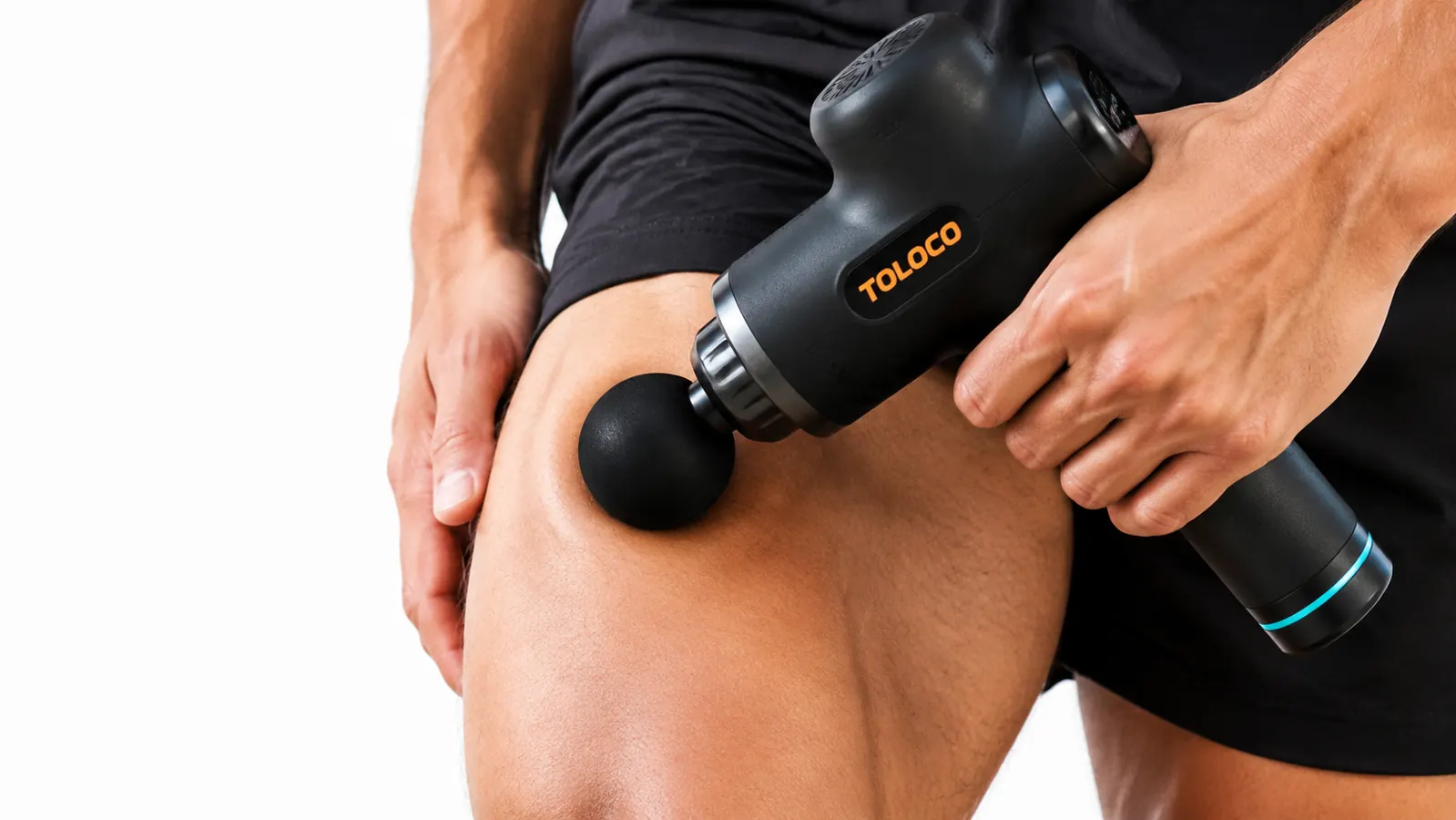 Hand holding the TOLOCO massage gun with the round ball attachment against a quad muscle