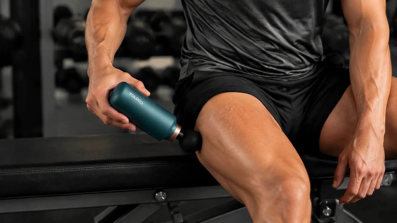 Hand holding the TOLOCO massage gun and pressing the ball attachment against an outer quad